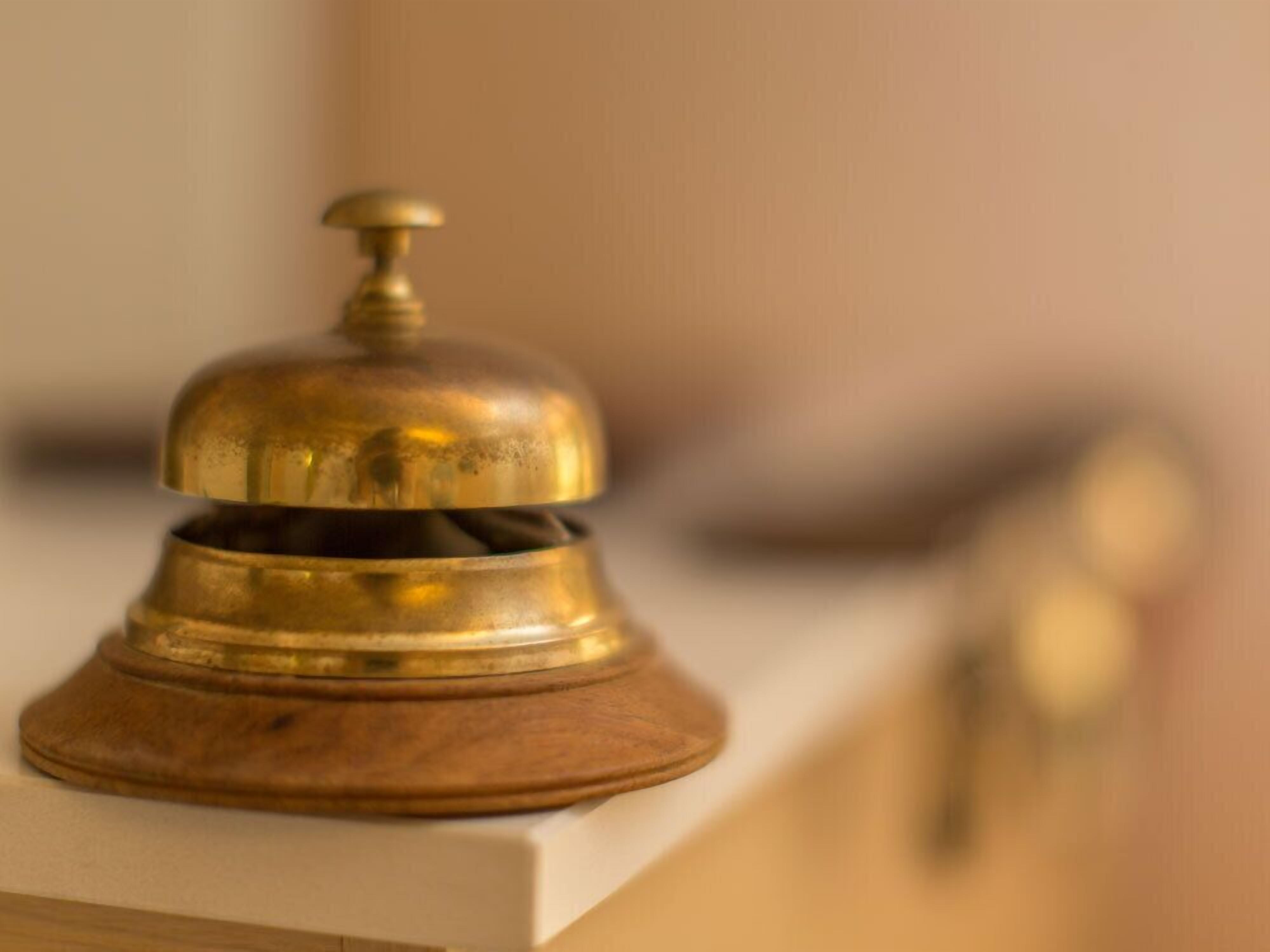 A brass bell on a wooden base, likely used for room service or guest announcements.