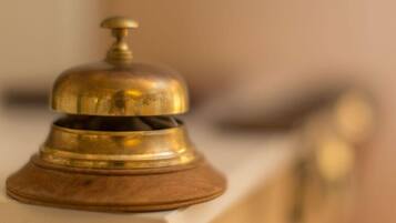 A brass bell on a wooden base, likely used for room service or guest announcements.