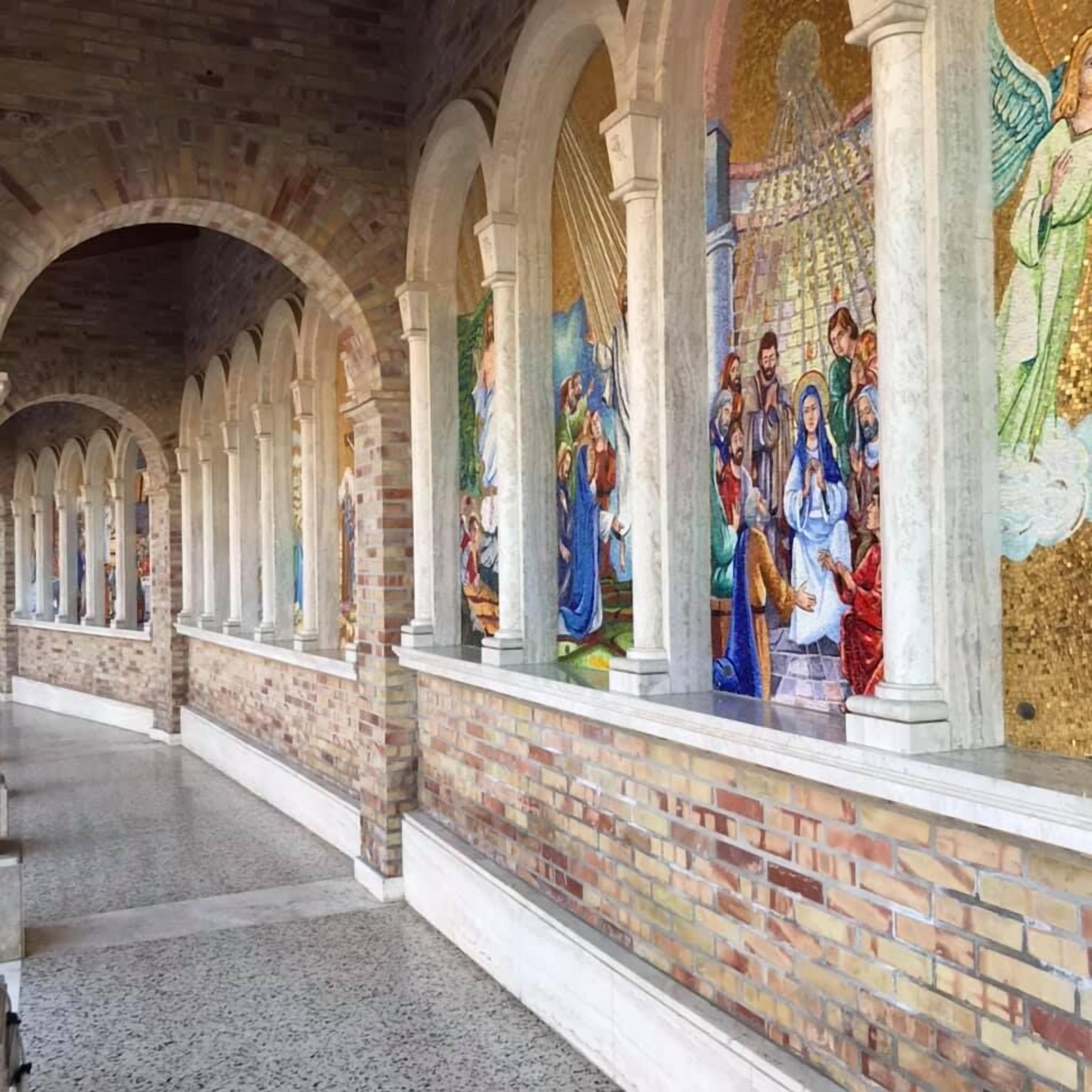 Een gang met gewelfde plafonds en een mozaïekmuur waarop religieuze figuren afgebeeld zijn.