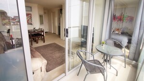 Ein modernes Wohnzimmer mit Glastür zum Balkon, einem Essbereich mit Tisch und Stühlen sowie einem Sofa.