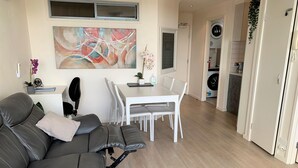 Ein modernes Wohnzimmer mit Ledersofa, einem Esstisch mit Stühlen, einem Gemälde an der Wand und einem Waschbereich im Hintergrund.