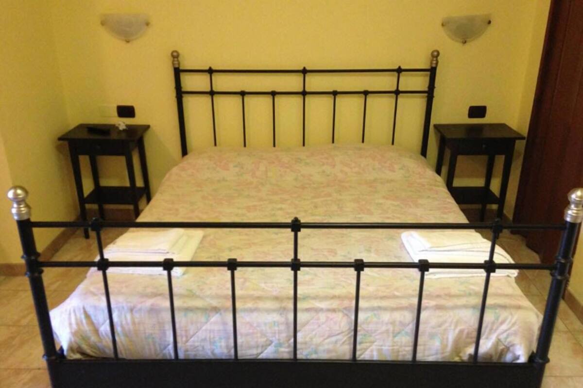 Una cama individual con estructura metálica, una colcha estampada y dos mesitas de noche con lámparas.