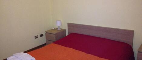 Una habitación de hotel con una cama individual, una mesita de noche con lámpara y una cómoda pequeña.
