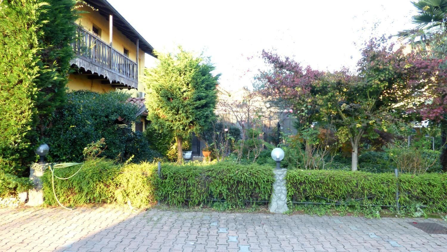 A paved courtyard with a hedge, a spherical lamp post, and a building with a balcony.