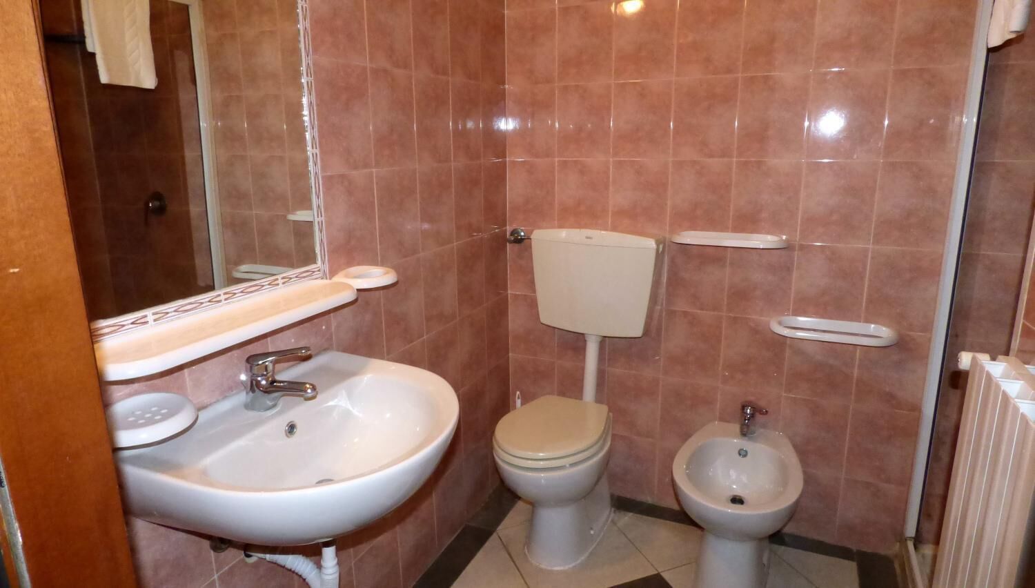 A bathroom with a sink, toilet, bidet, and tiled walls.