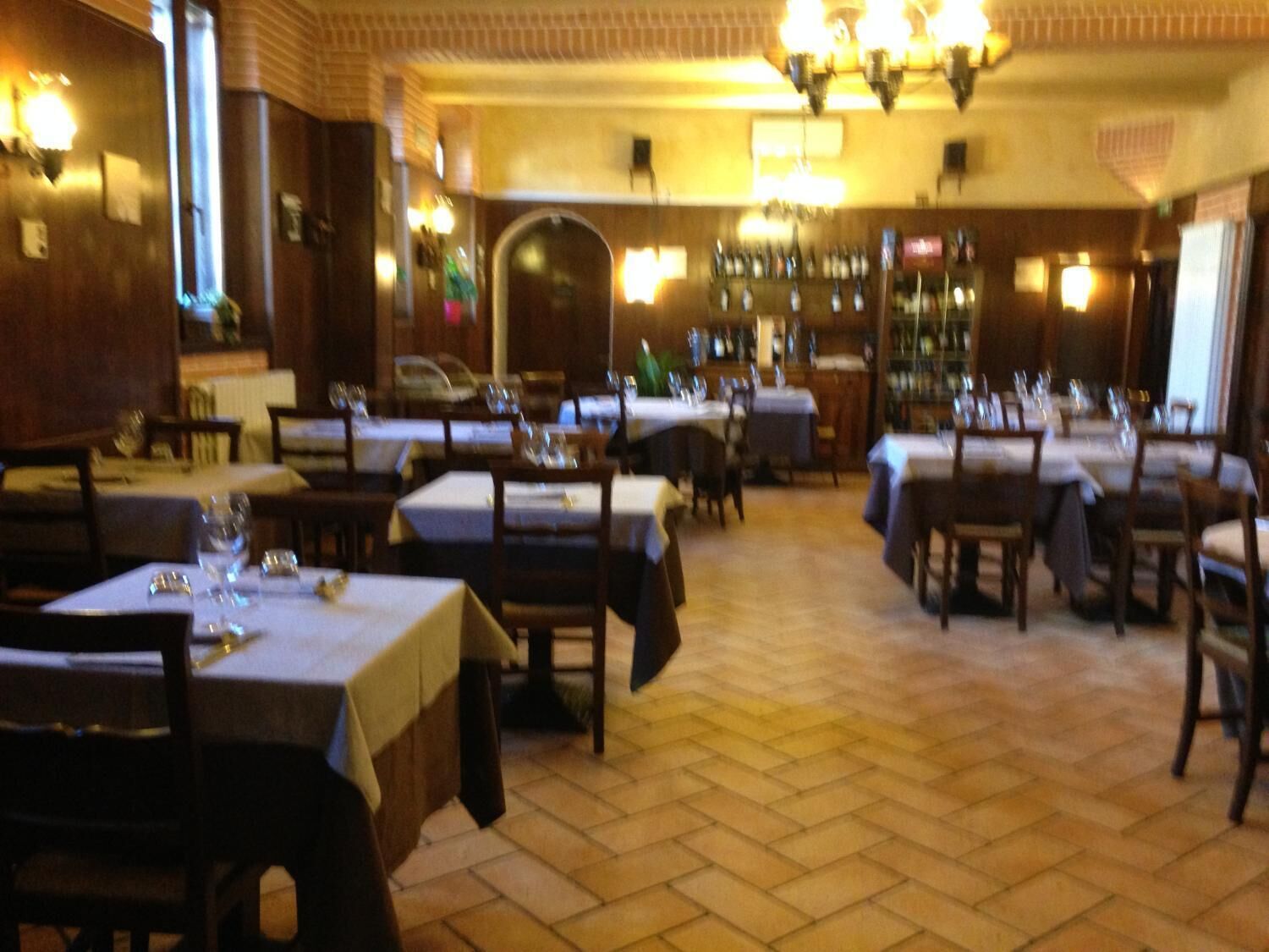 Un restaurant avec plusieurs tables et chaises, un bar avec des bouteilles et un mur en briques.