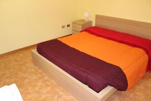 A bed with a wooden frame, a red and orange bedspread, and a small bedside table with a lamp. - La Pergola (Zibido San Giacomo)