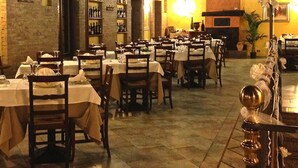 A restaurant with multiple tables and chairs, wooden beams on the ceiling, and shelves with bottles. - La Pergola (Zibido San Giacomo)