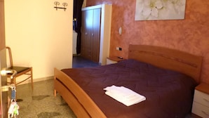 A bedroom with a wooden bed, a nightstand, a chair, a wardrobe, and a painting of flowers on the wall. - La Pergola (Zibido San Giacomo)