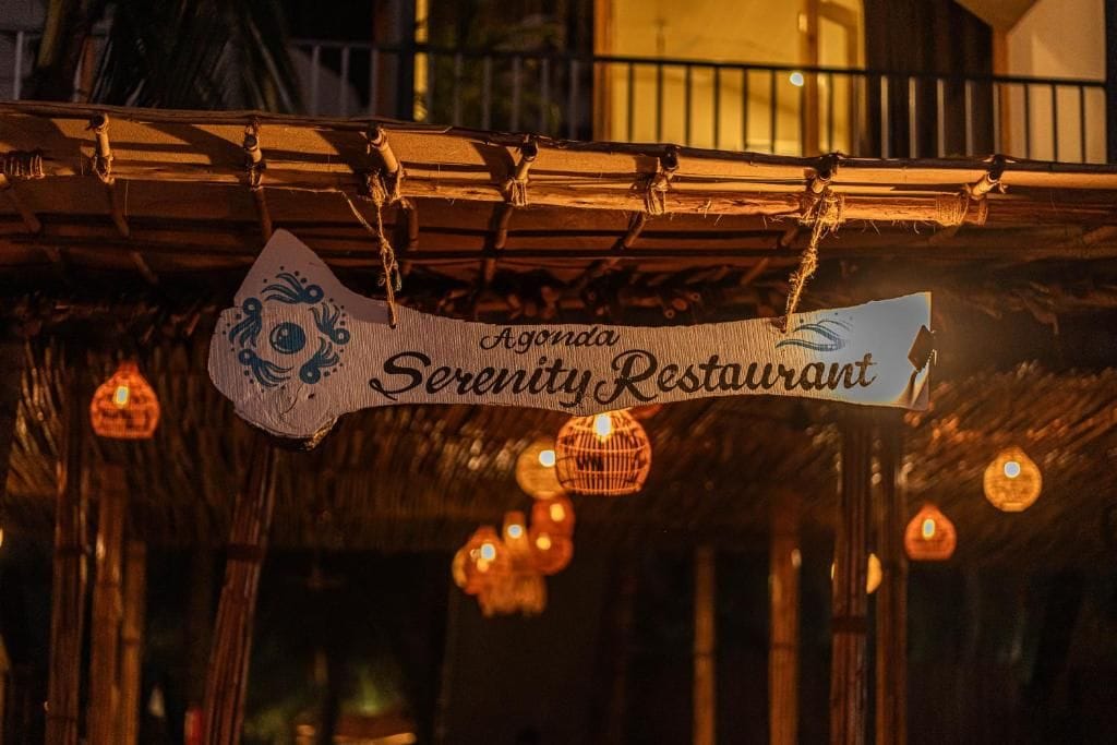 A sign for 'Agonda Serenity Restaurant' hanging from a bamboo structure.