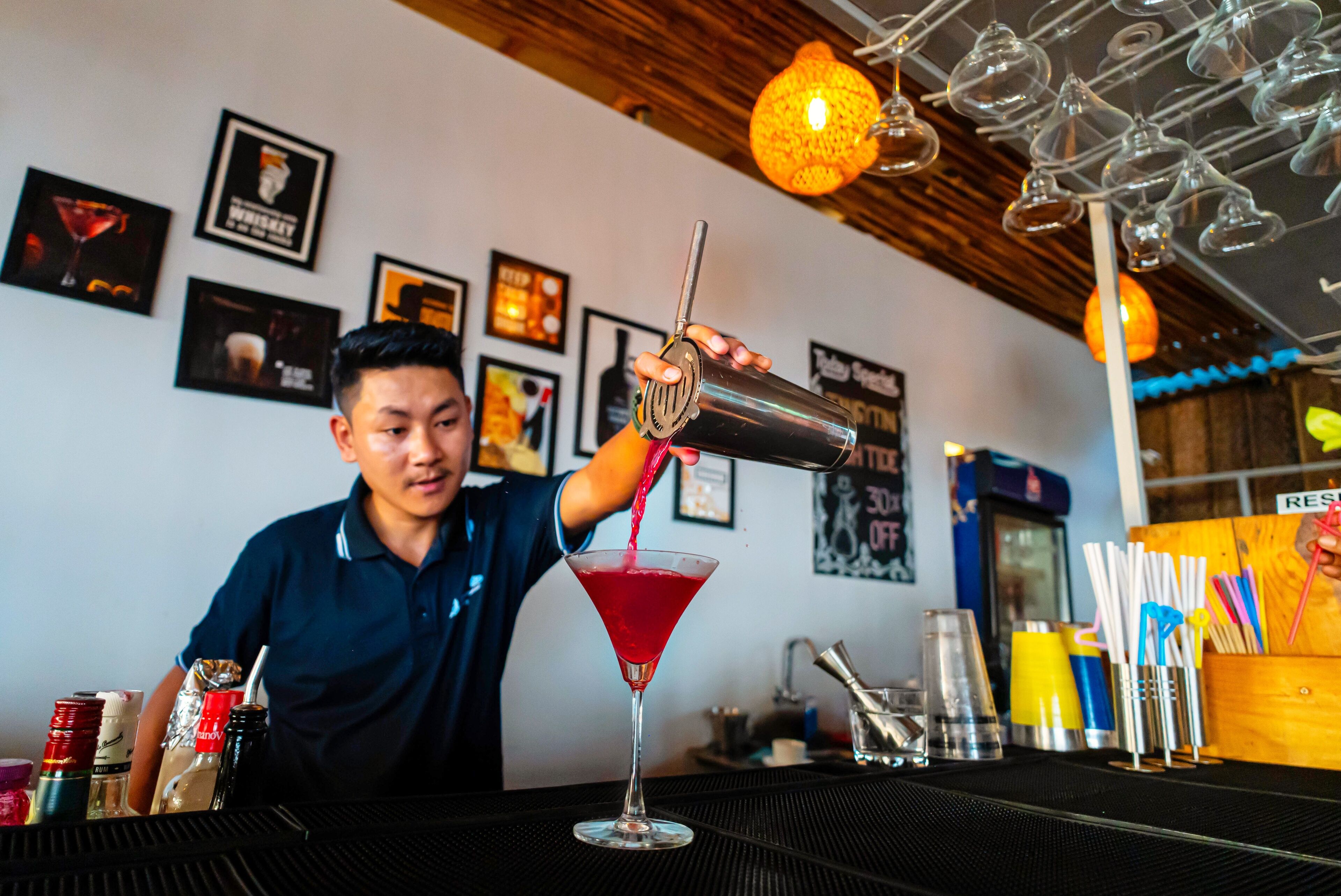 A bartender pouring a drink into a martini glass.