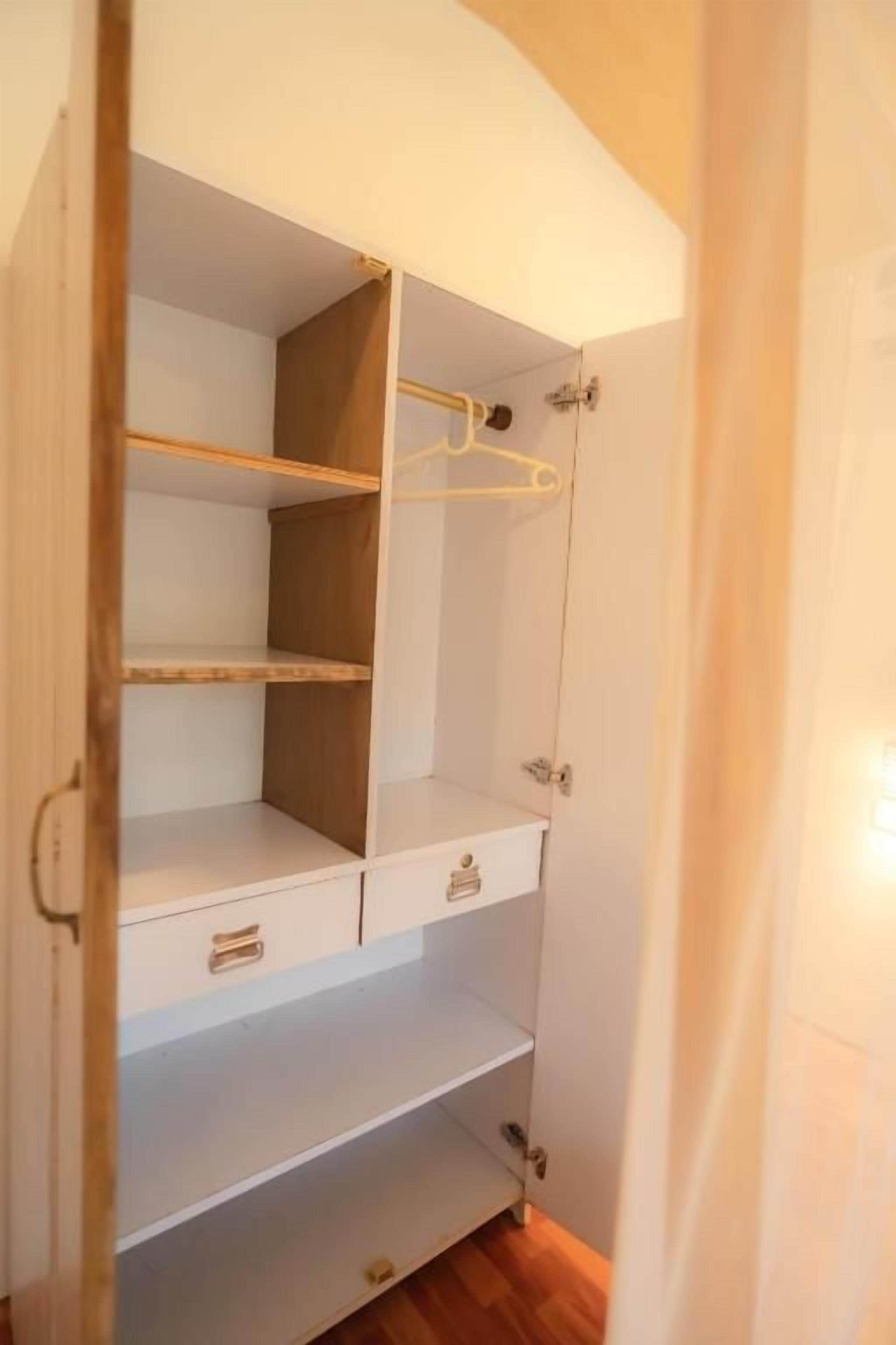 A walk-in closet with open doors, wooden shelves, and a hanging rod.