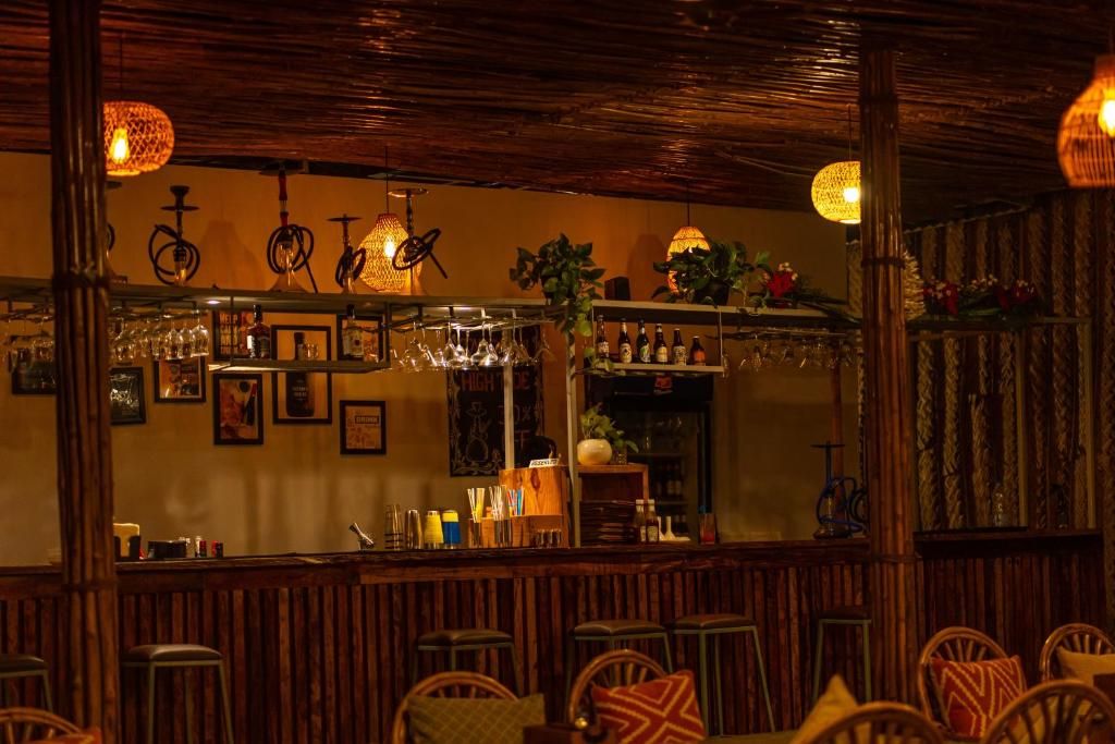 A bar area with wooden furniture, hanging lights, and shelves with bottles and glasses.