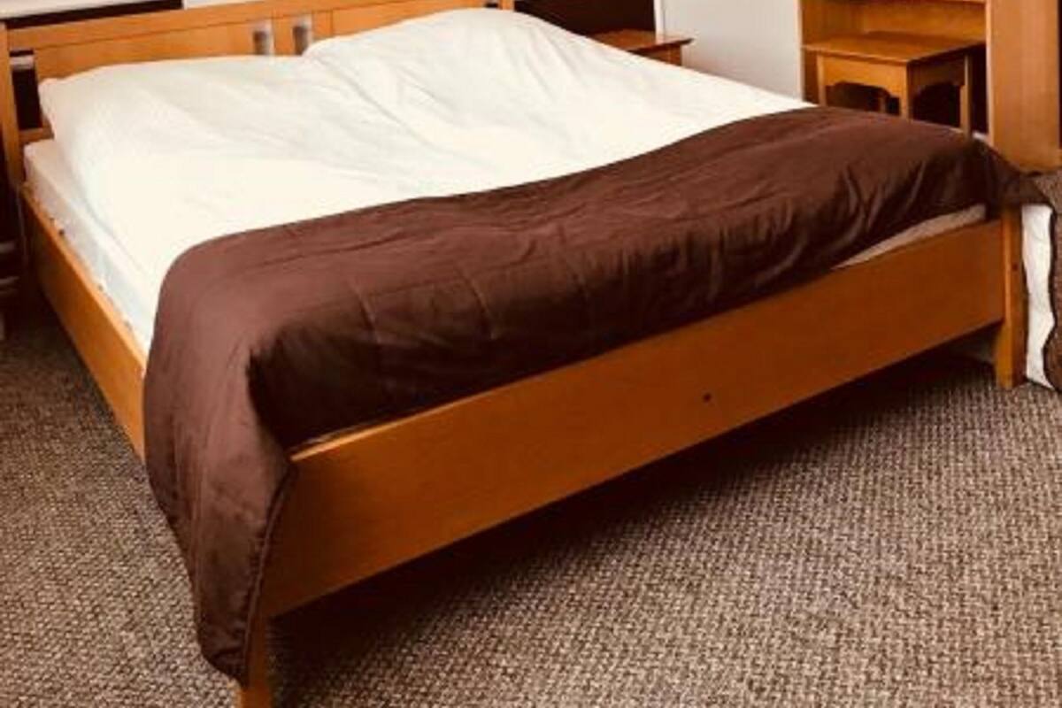 Ein Schlafzimmer mit einem hölzernen Bett, einem Nachttisch, einer Kommode und einem Spiegel.