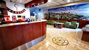 Un espace d’accueil avec un comptoir en bois, des drapeaux, une horloge et une fresque représentant Grenade.
