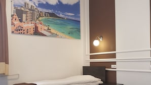 Une chambre d’hôtel avec un lit, une table de chevet, une lampe fixée au mur et une grande fresque représentant une plage.