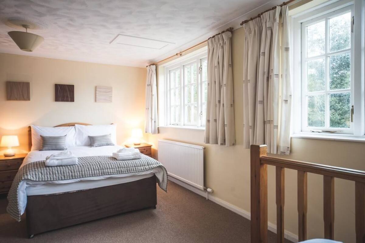 Une chambre bien rangée, avec un lit, des tables de chevet, un radiateur et une fenêtre avec des rideaux.