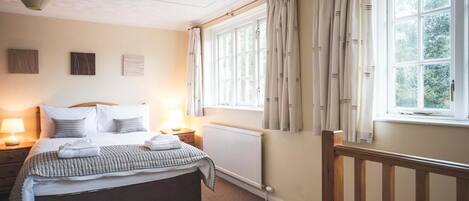 A neatly arranged bedroom with a bed, bedside tables, a radiator, and a window with curtains.