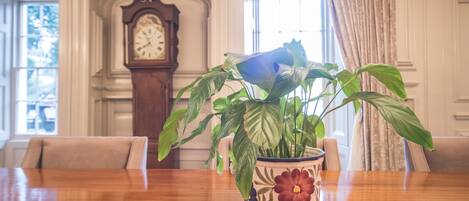 A wooden table with a floral vase containing a plant. A grandfather clock is in the background.