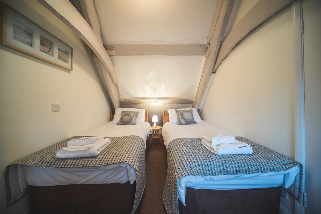 Een kleine, gezellige kamer met twee eenpersoonsbedden, een nachtkastje met lamp en een plafondlamp.