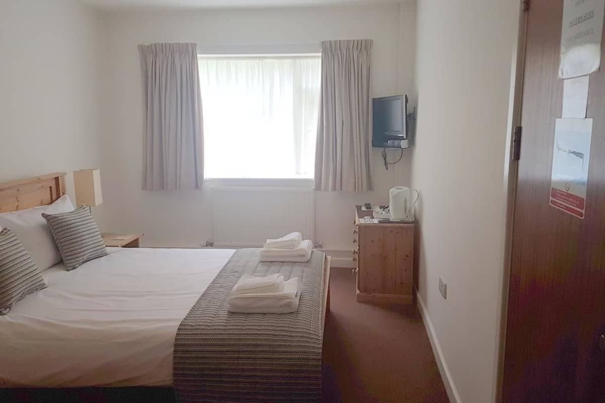 Une chambre d’hôtel avec un lit, une télévision, un bureau avec une lampe et une fenêtre avec des rideaux.