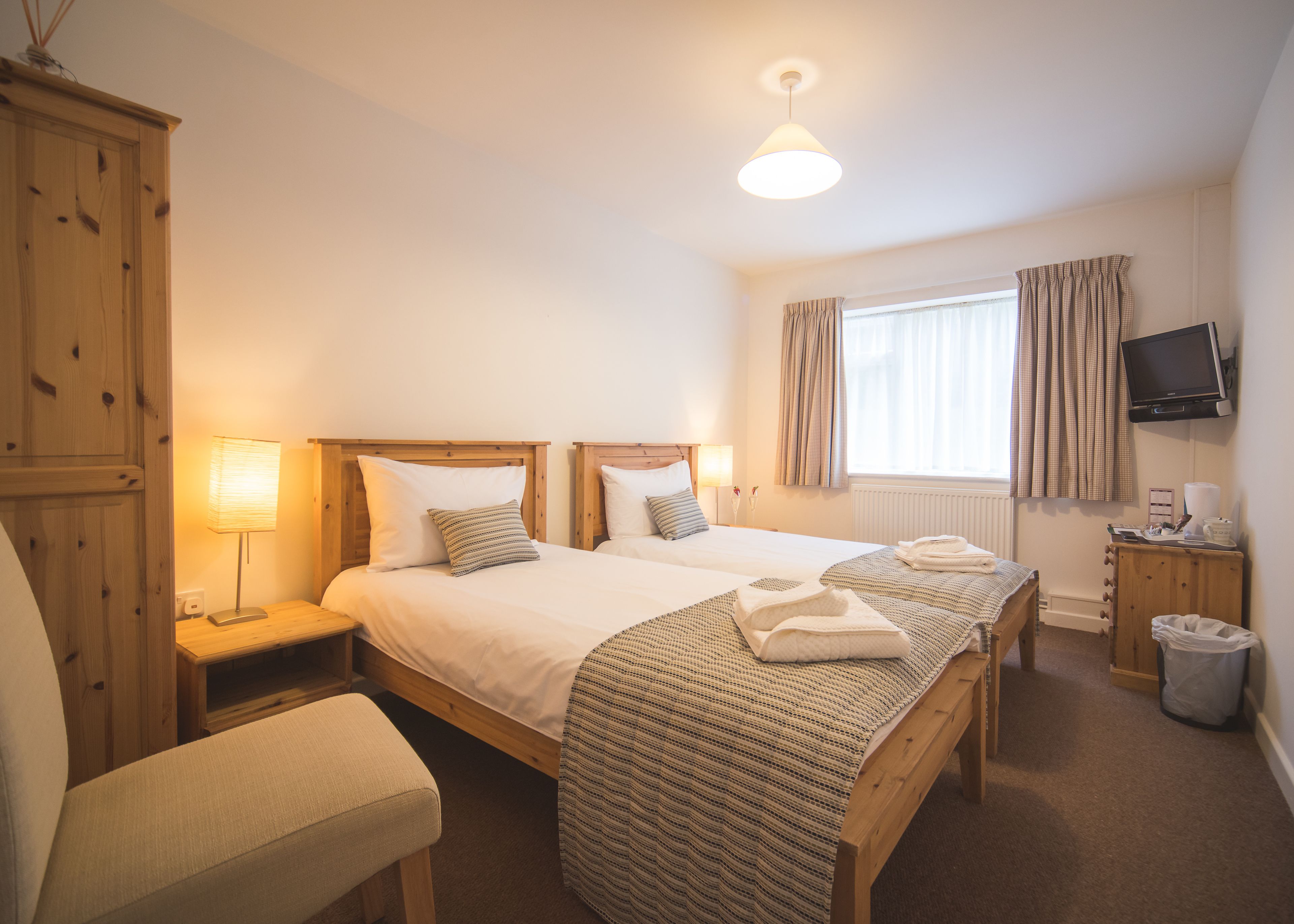 Een hotelkamer met twee bedden, een houten garderobe, een televisie en een raam met gordijnen.