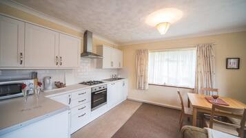 A compact kitchen with white cabinets, a stove, and a dining area with a table and chairs.