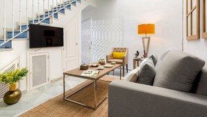 A living room with a sofa, a coffee table, a TV mounted on the wall, a staircase with blue tiles, and a patterned wall. - Genteel Home Casa Argote (Seville)