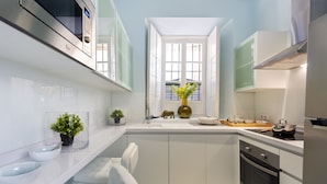 A modern kitchen with white cabinets, a built-in oven, and a window with blinds. - Genteel Home Casa Argote (Seville)