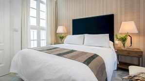 A hotel room with a large bed, two bedside tables with lamps, a window with curtains, and a wooden wall paneling. - Genteel Home Casa Argote (Seville)