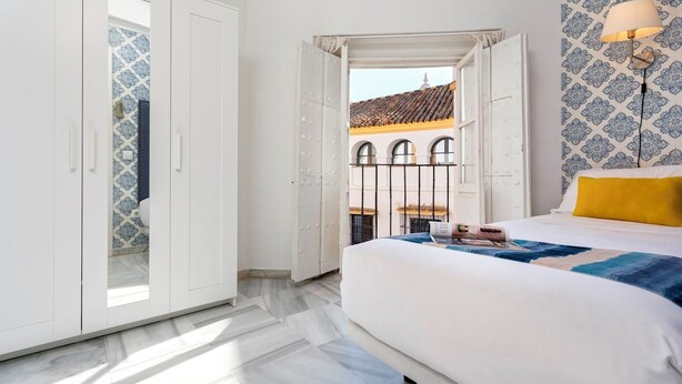 A bedroom with a bed, a wardrobe, and a view of a building with arches. - Genteel Home Casa Argote (Seville)