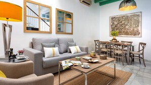 A modern living room with a grey sofa, wooden dining table, and chairs. There is a floor lamp, a magazine, and a cup on the coffee table. - Genteel Home Casa Argote (Seville)