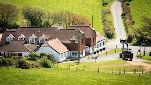A rural setting with a large building that appears to be a hotel or guesthouse, featuring multiple rooms with pitched roofs and a paved driveway. - The Chequers Inn (Ventnor)
