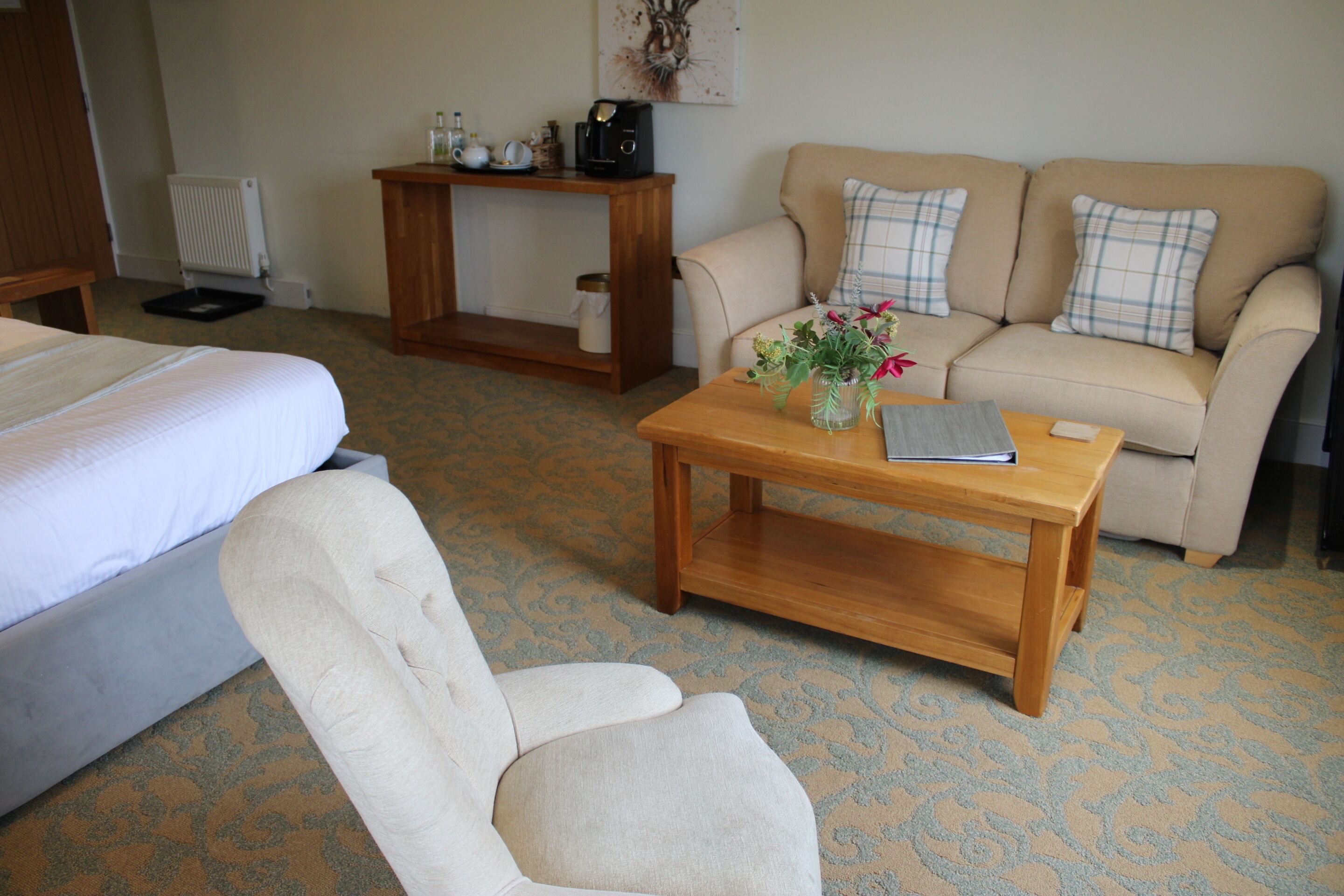 Une chambre d’hôtel avec un lit, un canapé, une table basse en bois et une petite table sur laquelle est posé un vase de fleurs.