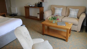 A hotel room with a bed, a sofa, a wooden coffee table, and a small table with a vase of flowers.