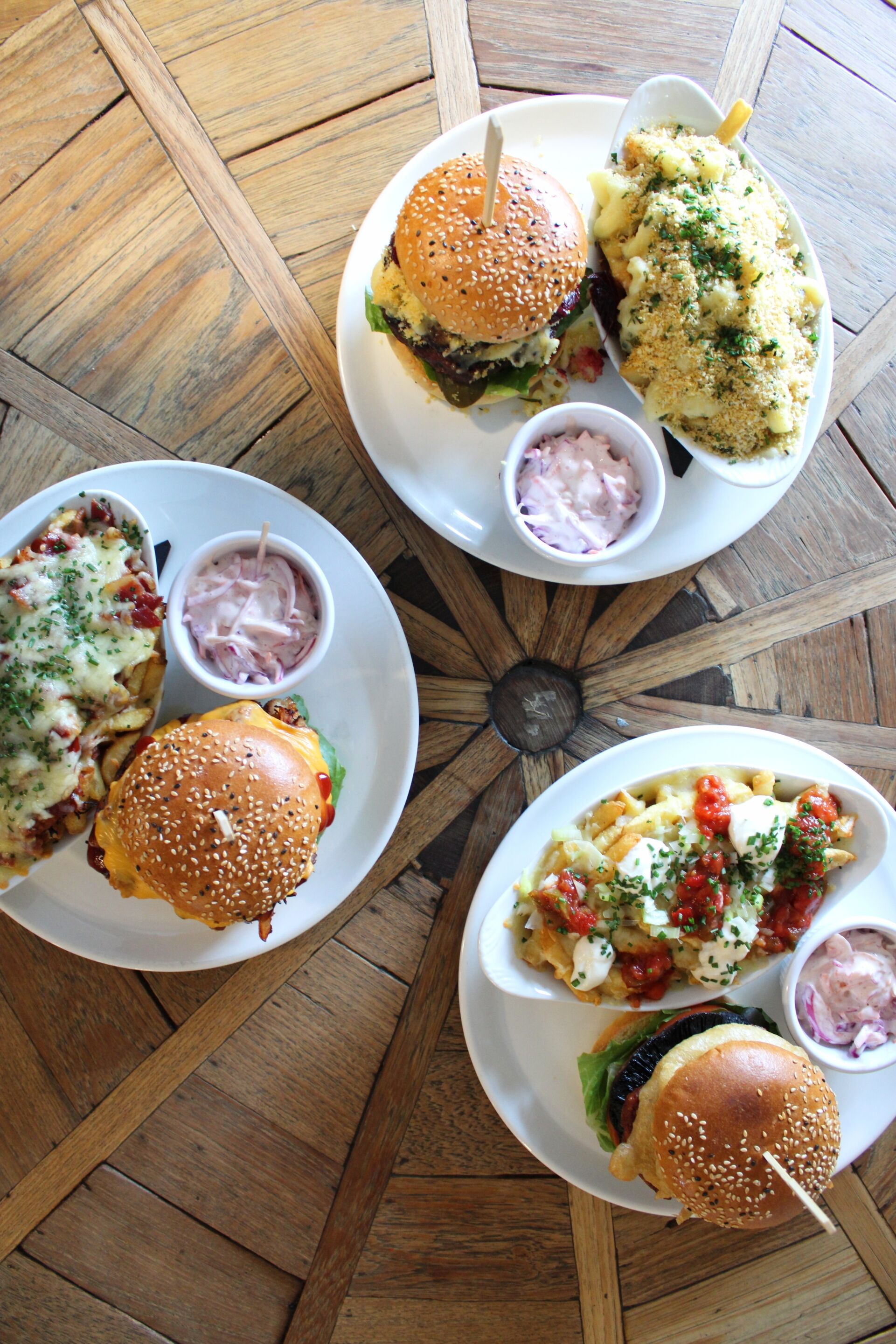 A dining table with four plates of food, including burgers and pasta dishes, and small bowls of dipping sauces.