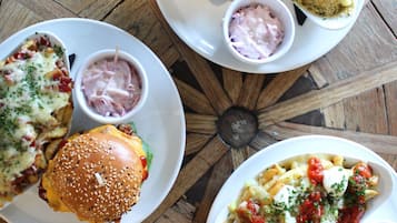A dining table with four plates of food, including burgers and pasta dishes, and small bowls of dipping sauces.
