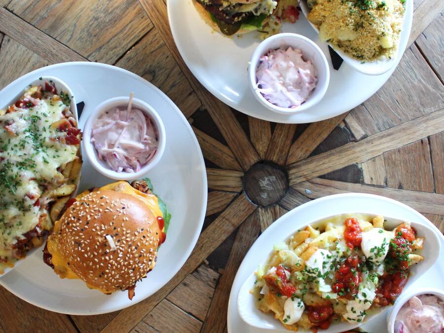 A dining table with four plates of food, including burgers and pasta dishes, and small bowls of dipping sauces.
