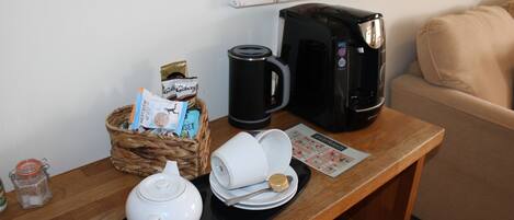A coffee station with a coffee maker, teapot, cups, and a basket of cookies.