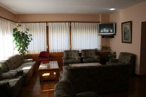 A living room with a sofa set, a red chair, a coffee table, and a television on a stand. - Hotel Escalar (Panticosa)