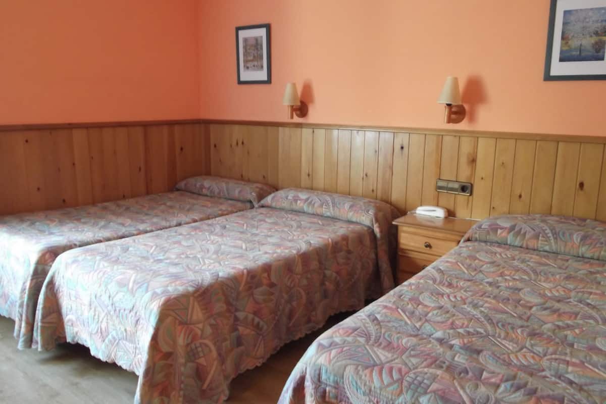 A room with three single beds, wooden headboards, and two wall-mounted lamps.