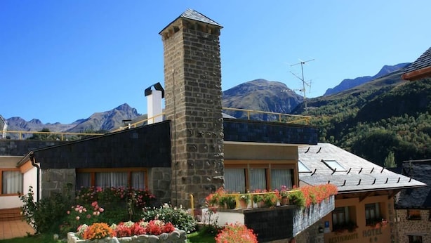 A stone building with a chimney, a balcony with potted plants, and a sign for a restaurant and hotel. - Hotel Escalar (Panticosa)