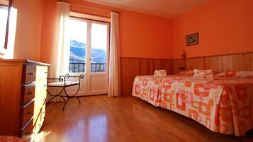 Un dormitorio con un aparador de madera, una cama con ropa de cama estampada, un ventanal con cortinas y vistas a la montaña.