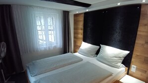 A double bed with a wooden headboard, a bedside table, and a window with curtains. - Hotel Corveyer Hof (Hoexter)