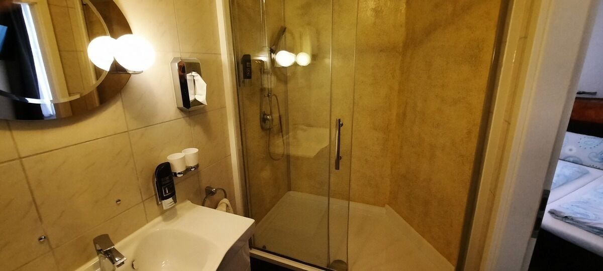 A bathroom with a glass-enclosed shower, a sink with a mirror, and a towel dispenser.
