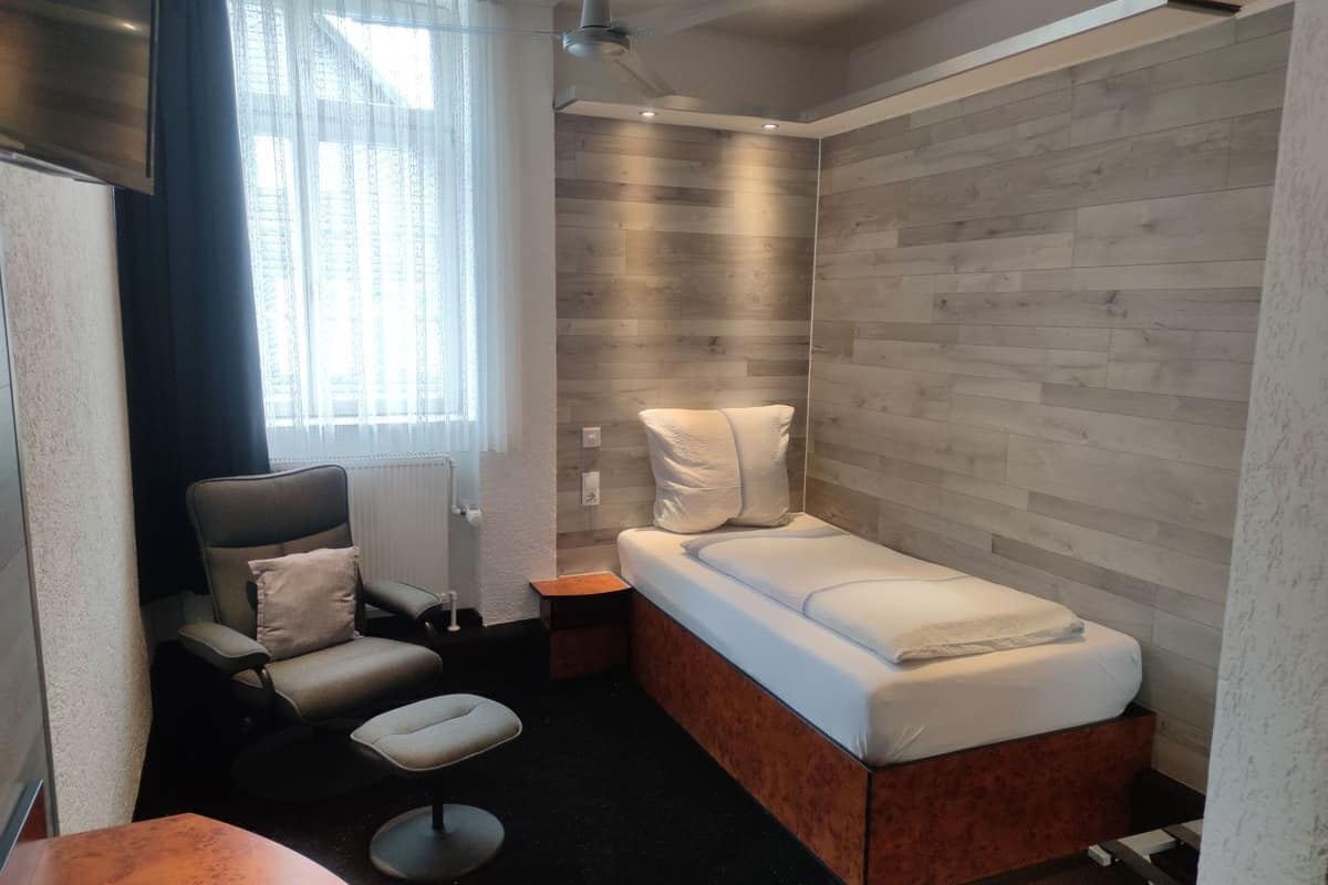 A compact room with a bed, a chair, a small table, and a window with curtains.