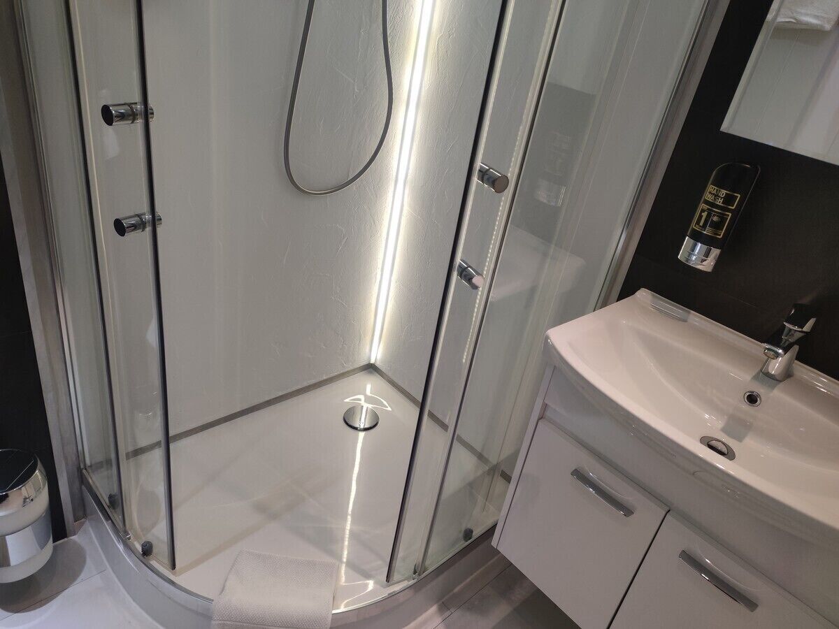A modern bathroom with a glass shower enclosure, a white sink, and a mirror.