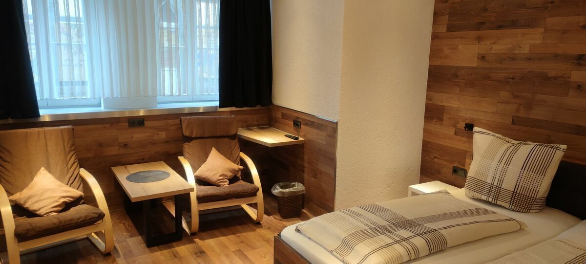 Una habitació d'hotel amb un llit, dues cadires, una taula petita i una finestra amb cortines.