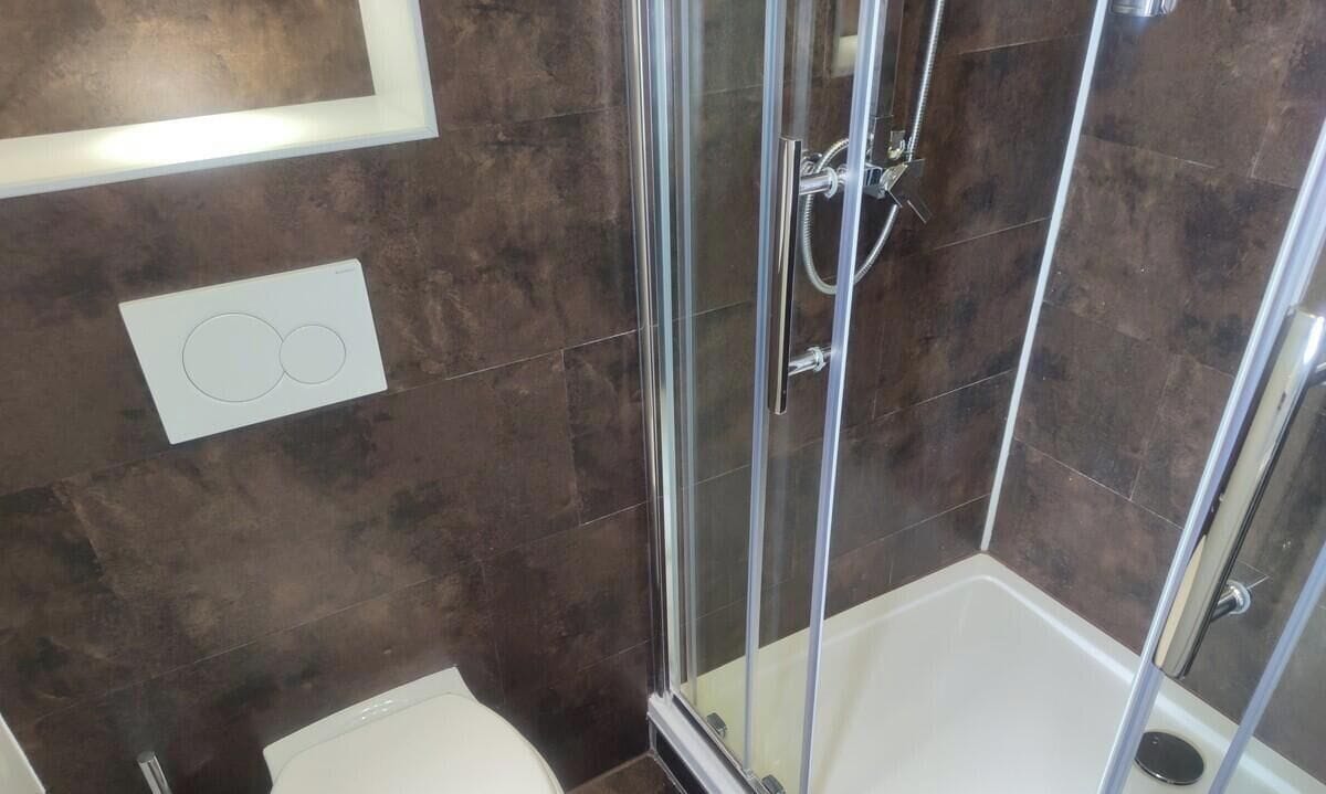 A shower with glass doors, a white bathtub, and a wall-mounted light fixture.
