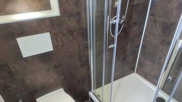 Ducha con puertas de vidrio, una bañera blanca y un aplique en la pared.